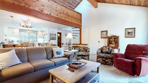 Een gezellige woonkamer met een bank, fauteuil en salontafel. In de achtergrond is een houten plafond en een trap te zien.