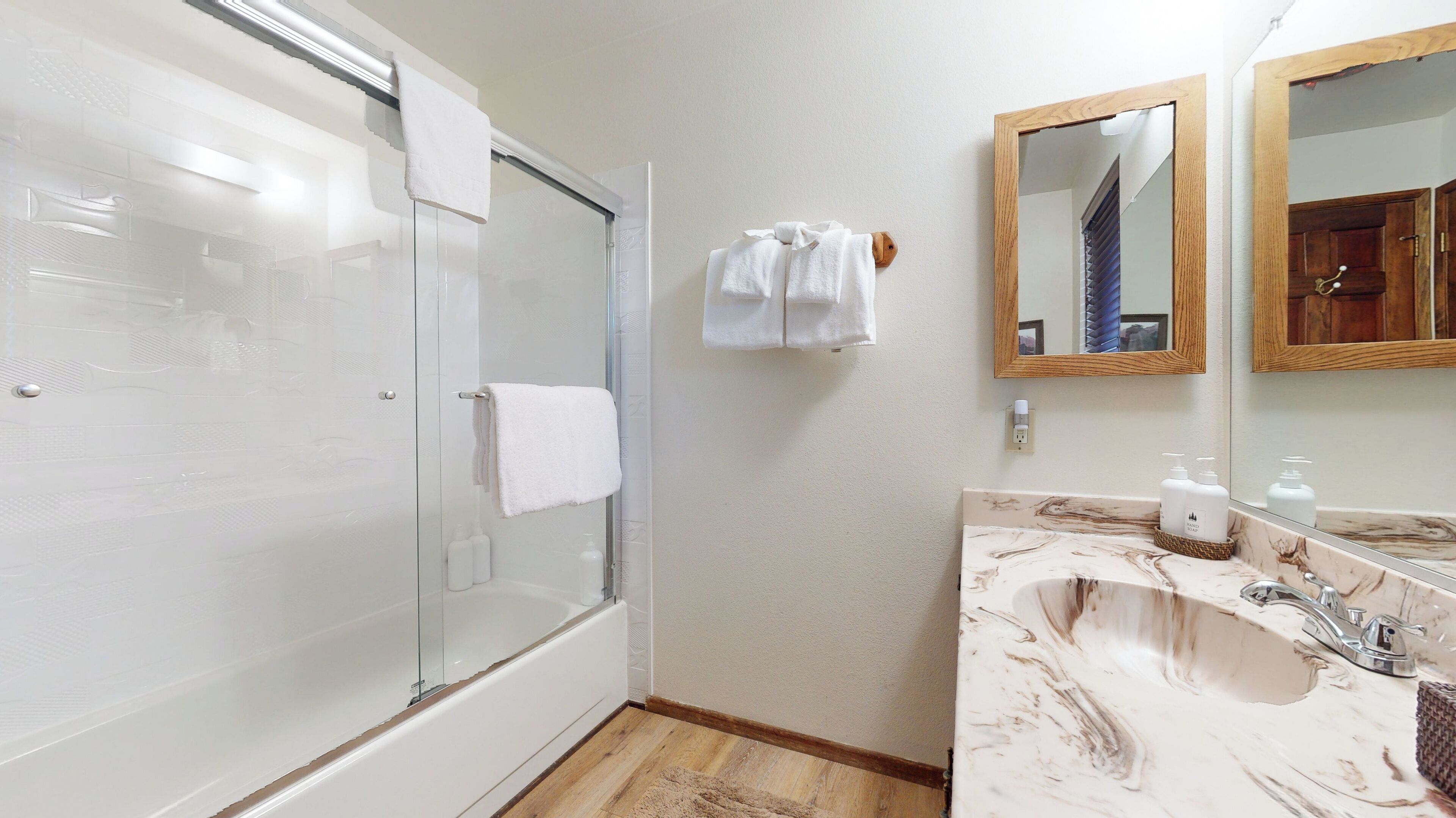 A bathroom with a glass-enclosed shower, a marble sink, and a wooden-framed mirror.
