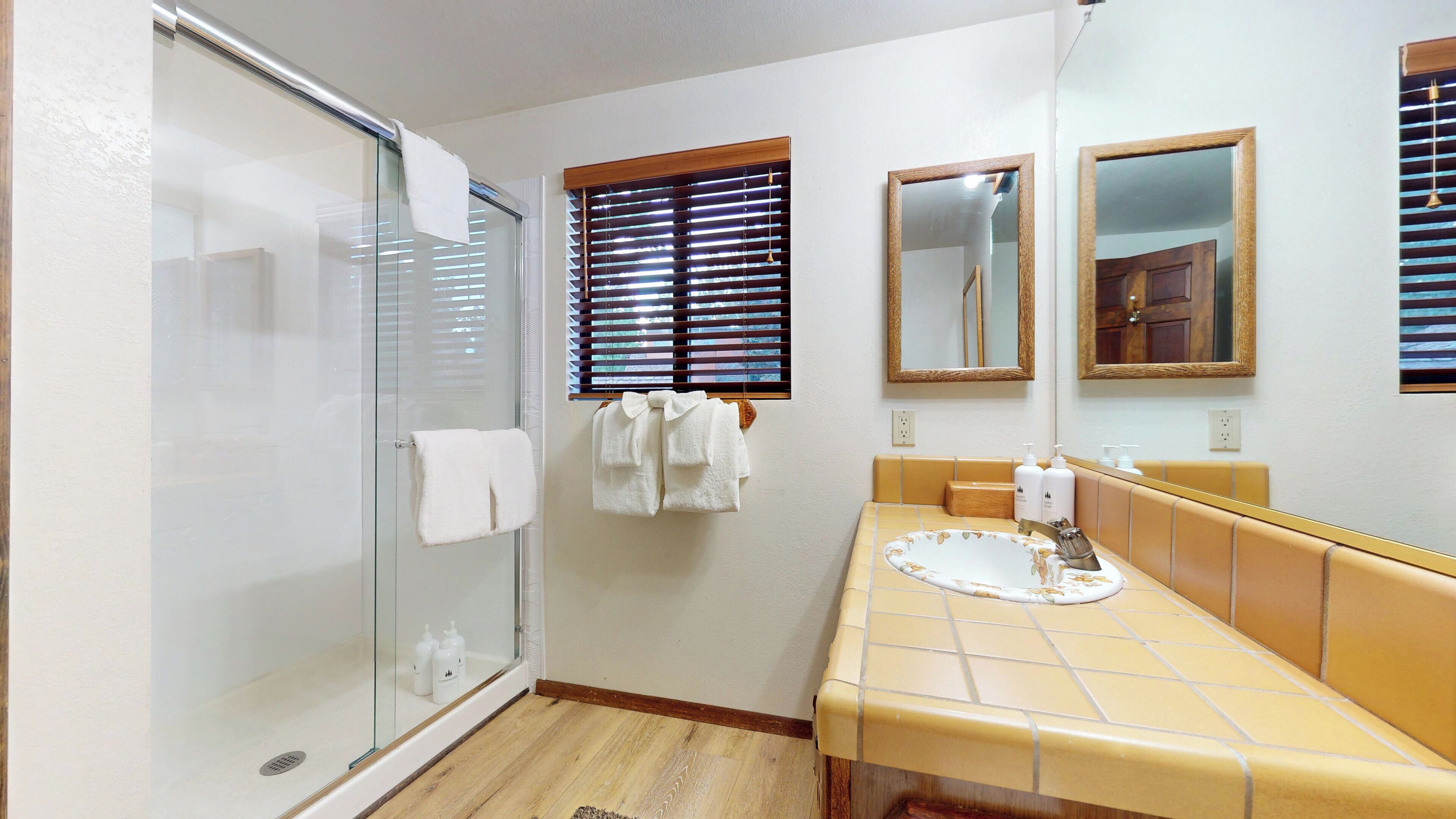 Une salle de bain avec une porte de douche en verre, un lavabo orné d’un motif floral et deux miroirs.
