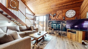 Una sala de estar acogedora con una escalera de madera, una chimenea de piedra y un televisor de pantalla plana grande.