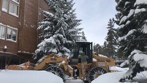 Een sneeuwruimer geparkeerd in een besneeuwd woongebied, met huizen en bomen op de achtergrond.