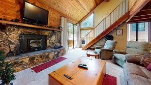 Una sala de estar acogedora con chimenea de piedra, un televisor de pantalla plana montado encima y un sofá confortable, además de una escalera que sube a un nivel superior.