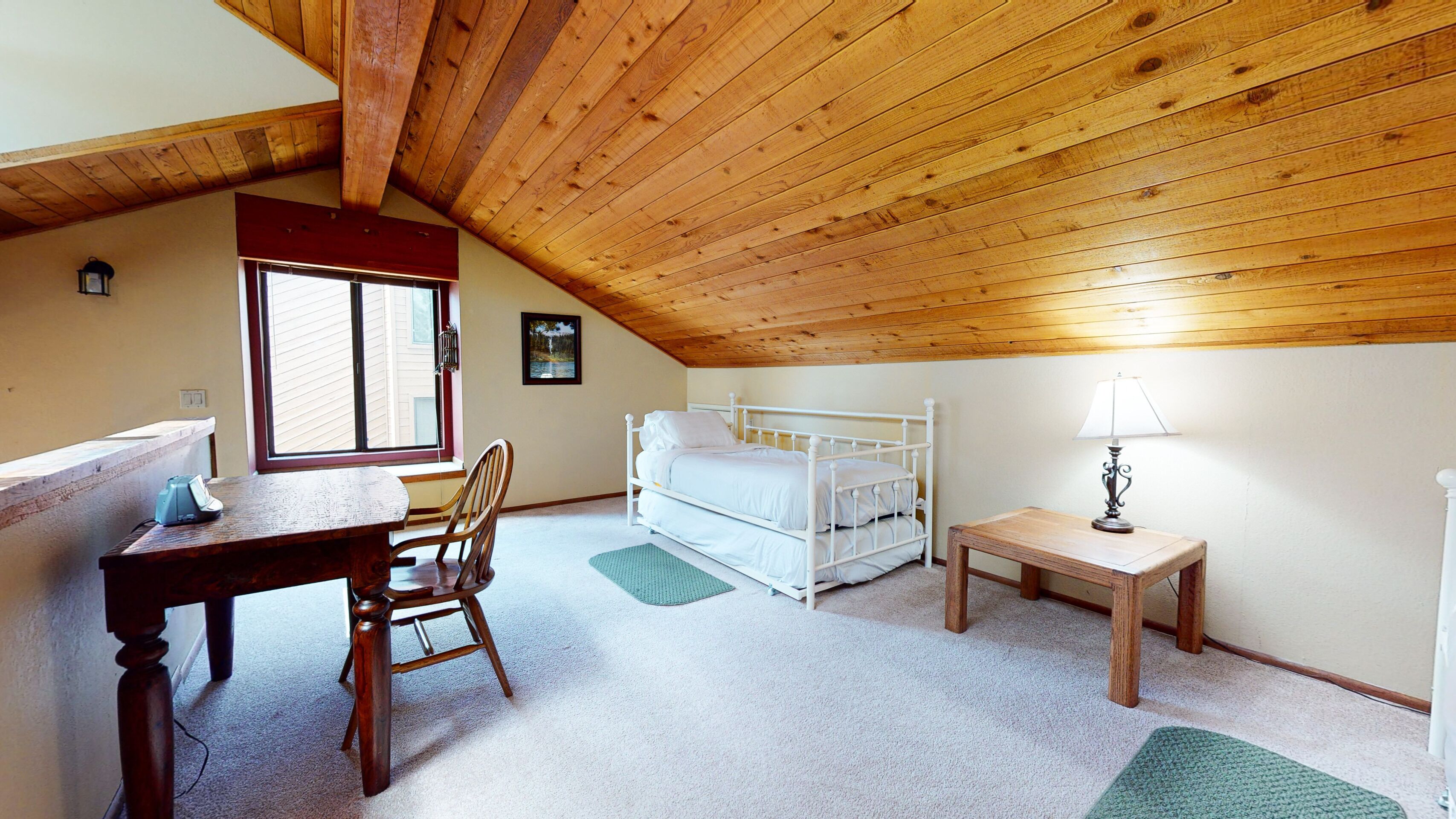 A cozy attic bedroom with a wooden ceiling, a single bed, a desk, and a chair.