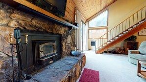A stone fireplace with a modern TV, a staircase, and a cozy living area with a red rug. - Mountain Rustic, Spacious. Washer/Dryer, On-site Pool & Near Trails/Kids Park (Mammoth Lakes)