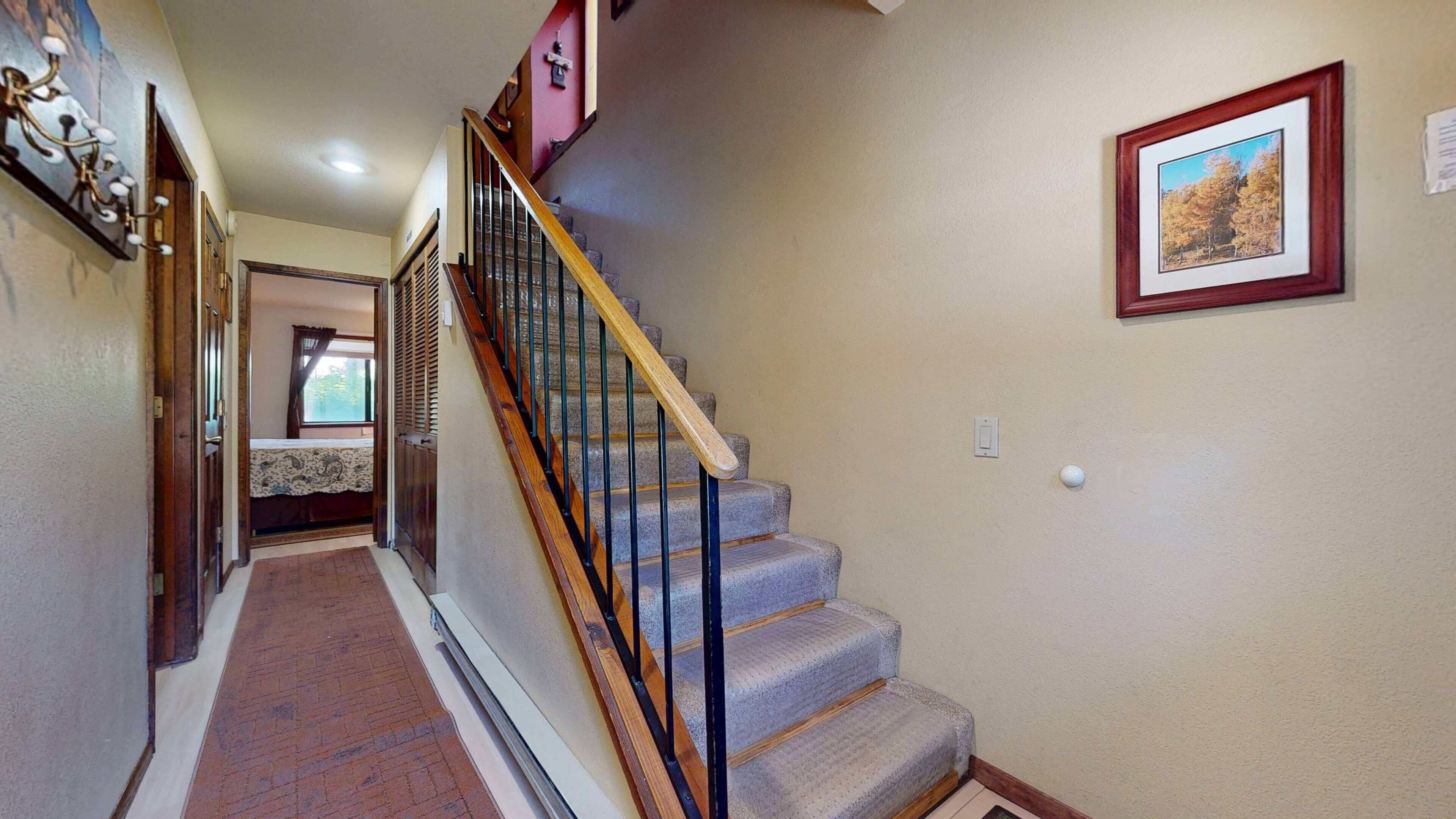 Una escalera con escalones de madera y barandillas de metal, que conduce a un dormitorio con ventana y cama.