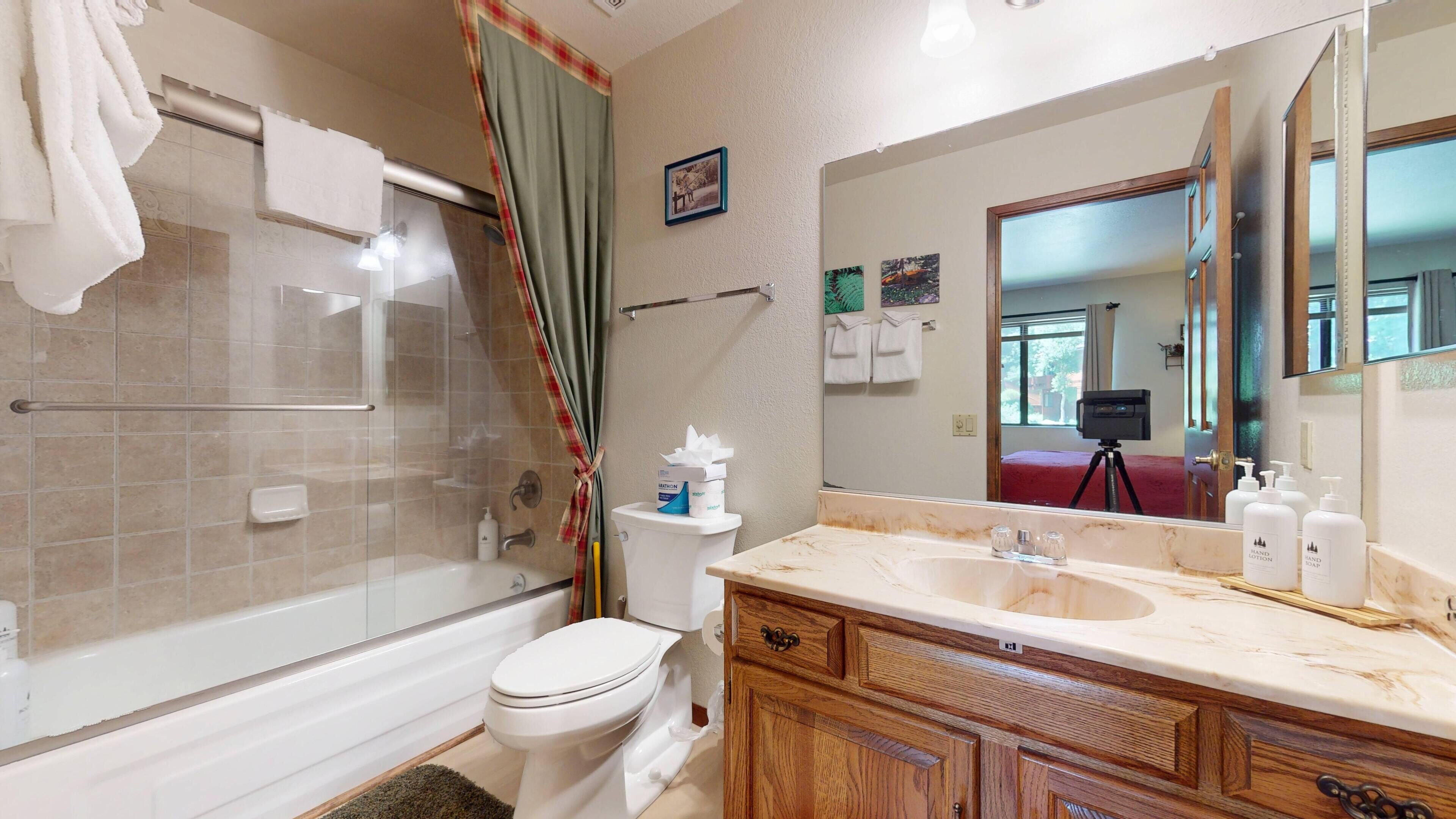 A bathroom with a glass-enclosed shower, a toilet, a vanity with a marble countertop, and a large mirror.