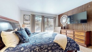 Un dormitorio con una cama grande, un aparador de madera, un televisor y una ventana con vistas al exterior.