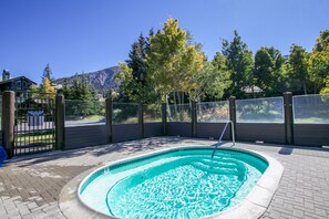 Ein Schwimmbecken mit einer gefliesten Kante, umgeben von einer Pflasterterrasse und einem Holzzaun mit einem Tor.