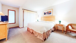 Ein Hotelzimmer mit einem großen Bett, einem Schreibtisch mit Computer, einem Stuhl, einem Fenster mit Vorhängen und einem Bild an der Wand.