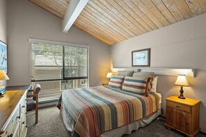A bedroom with a bed, bedside lamps, a wooden nightstand, a desk, and a chair.