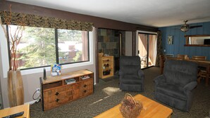 A living room with a large window, a fireplace, two armchairs, a wooden coffee table, and a TV on a wooden stand. - Mammoth Ski & Racquet Club #94, 2 bedroom Dog Friendly (Mammoth Lakes)