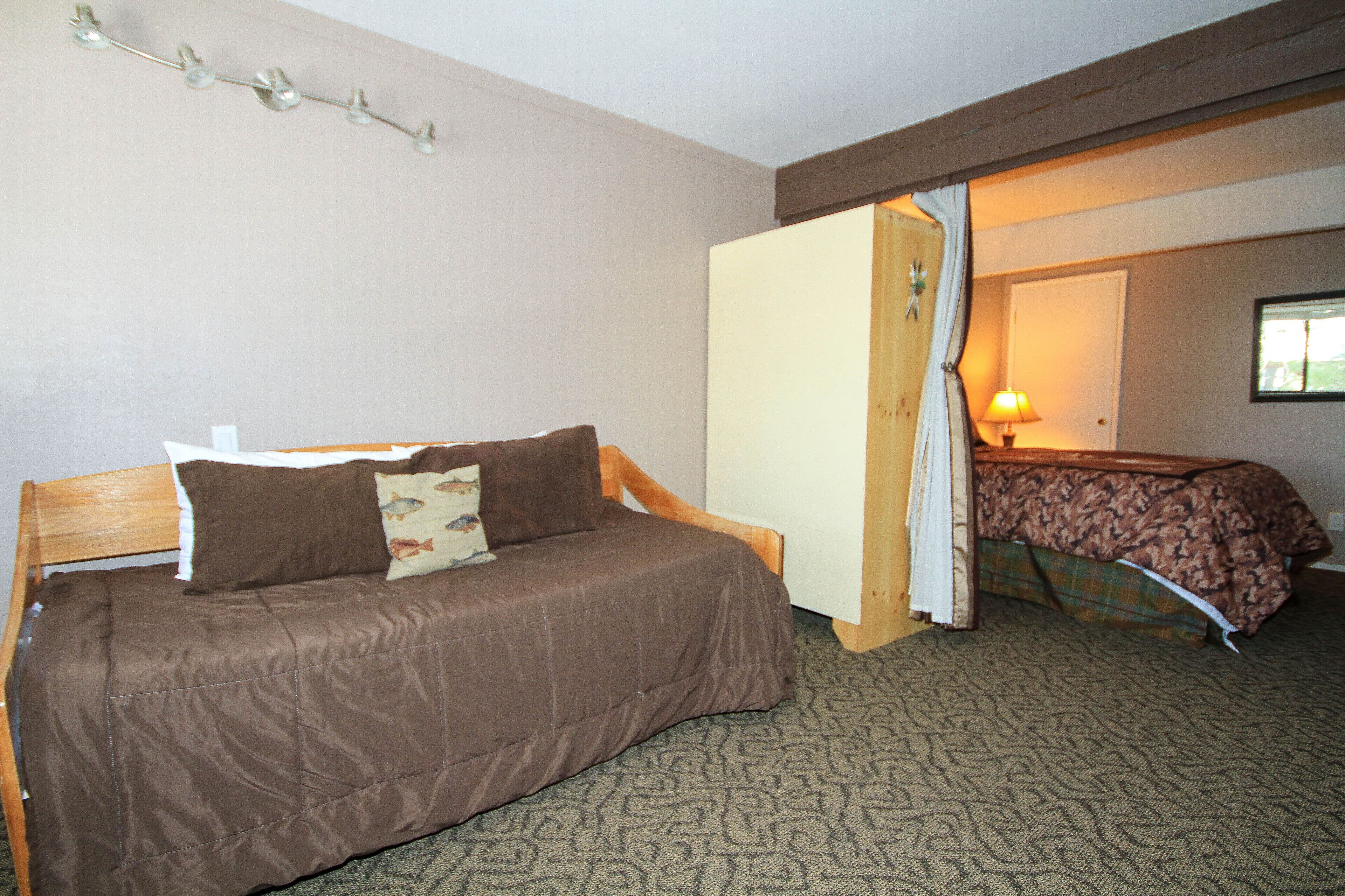 A bedroom with a wooden bed, a nightstand, a lamp, and a door leading to another room.