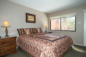 A bedroom with a bed, two bedside tables with lamps, a window with blinds, and a framed picture on the wall.