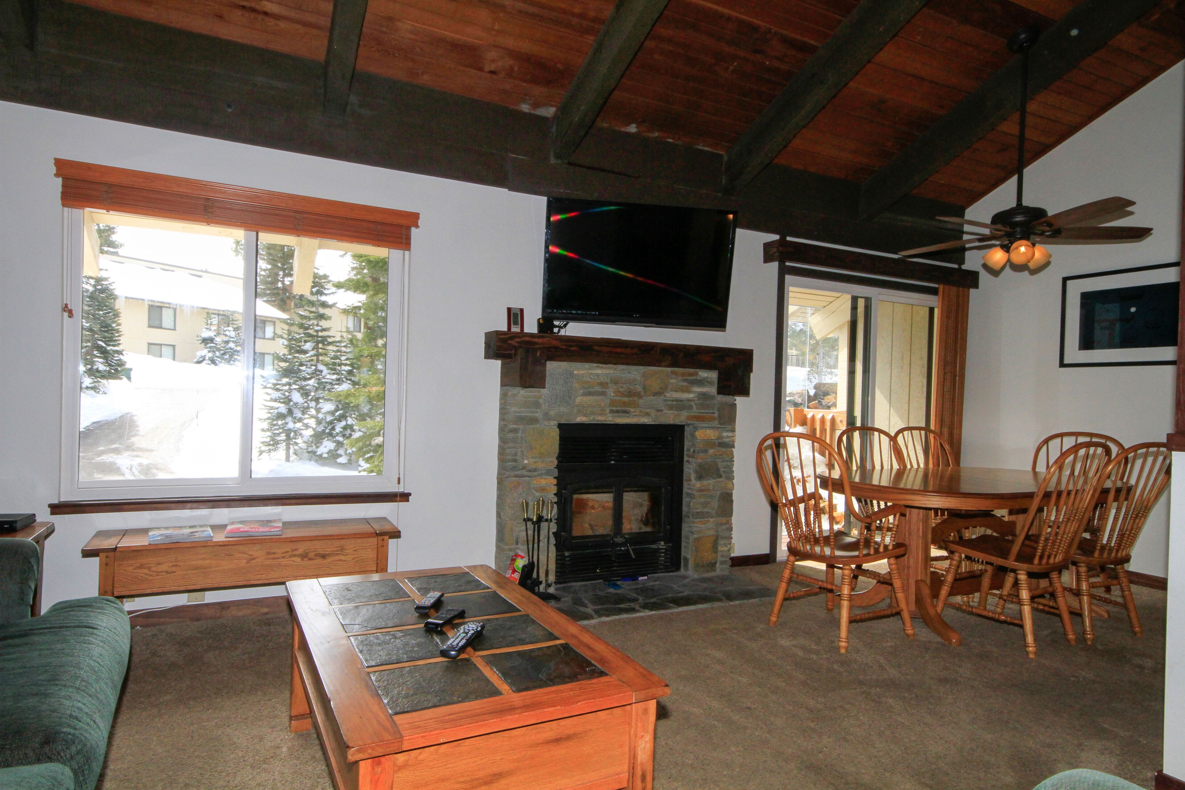 Un salón acogedor con chimenea, un televisor montado sobre ella y una zona de comedor con muebles de madera.