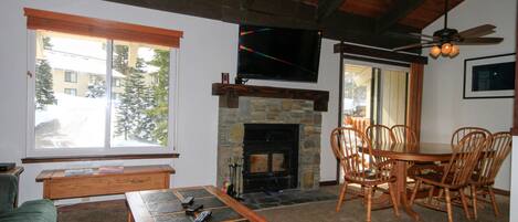 Un salón acogedor con chimenea, un televisor montado sobre ella y una zona de comedor con muebles de madera.
