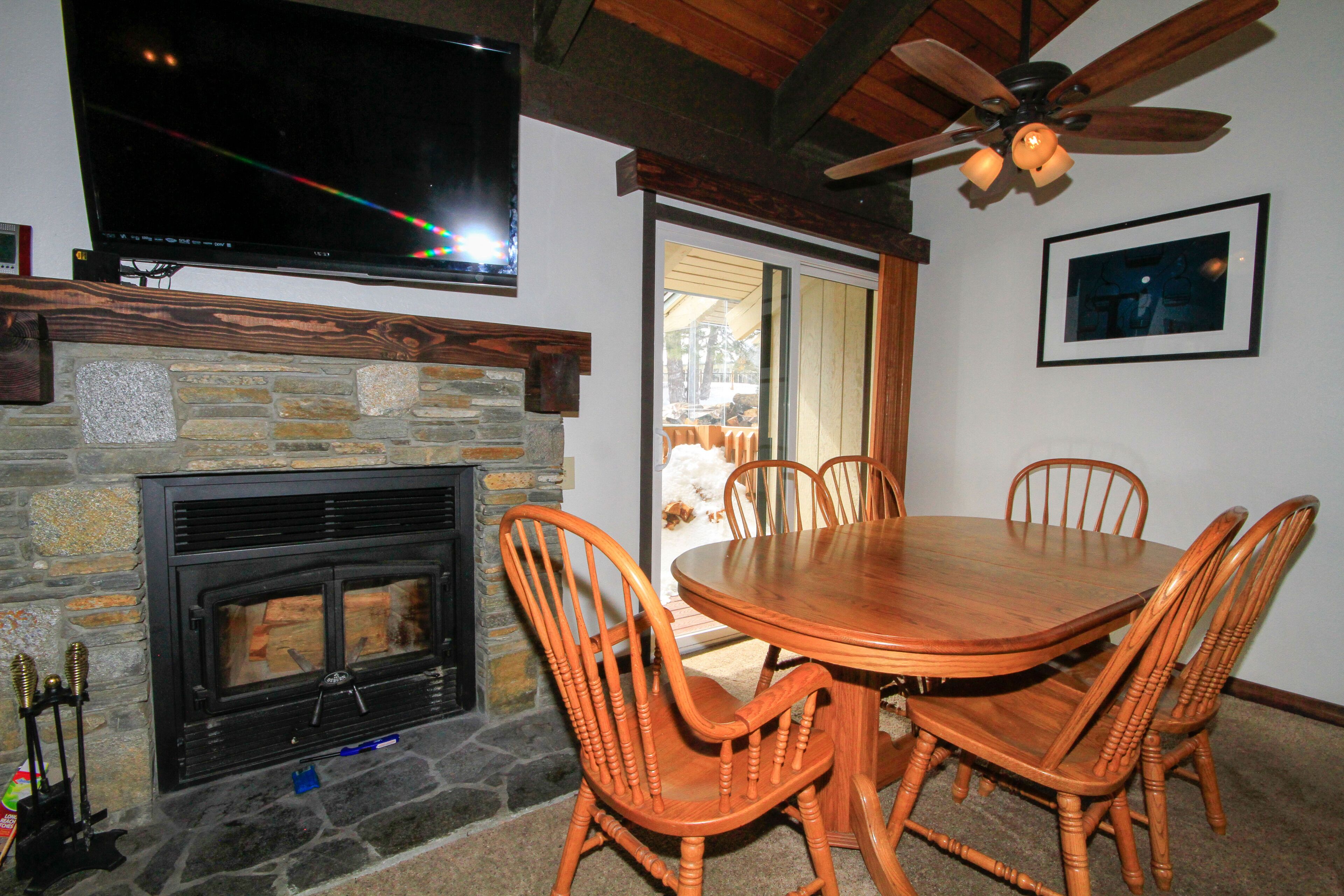 A dining area with a stone fireplace, wooden chairs, and a ceiling fan.