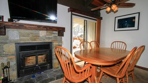 Un comedor con chimenea de piedra, sillas de madera y un ventilador de techo.