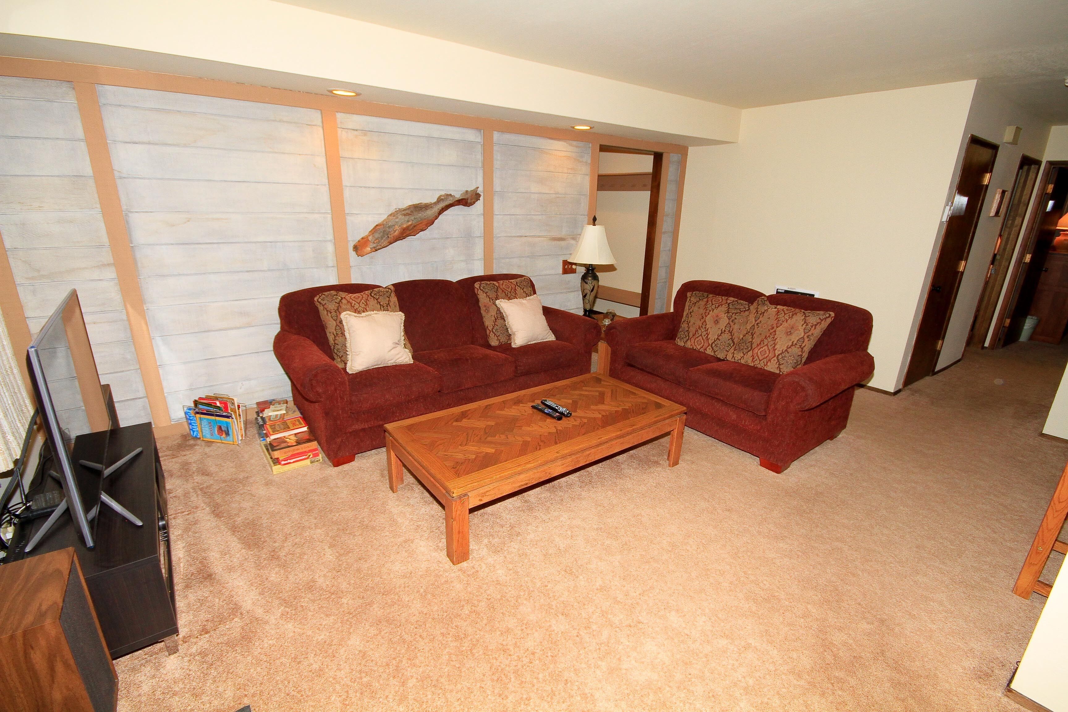 Ein Wohnzimmer mit zwei roten Sofas, einem Holztisch und einem Fernseher auf einem Schrank.
