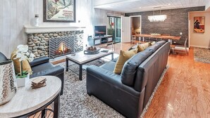 A modern living room with a stone fireplace, leather sofa, and a dining area with a wooden table and chairs.