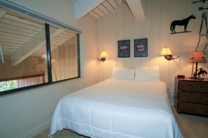 A bedroom with a large bed, two wall-mounted lamps, a wooden dresser, and a window with blinds. - Mammoth Ski & Racquet Club #67- (Mammoth Lakes)