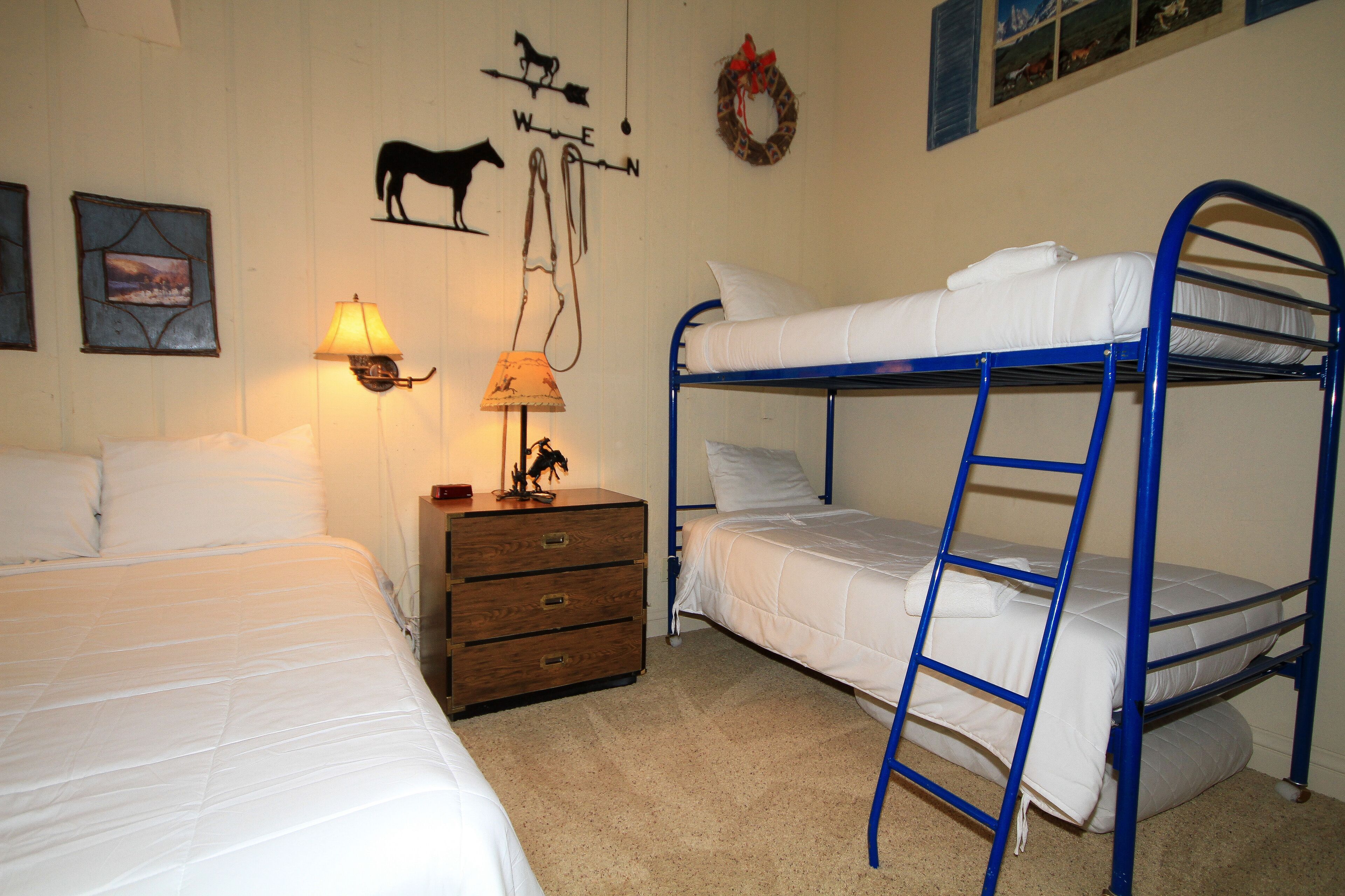 A room with a bunk bed, a wooden dresser, a lamp, and wall decorations including a compass and animal silhouettes.