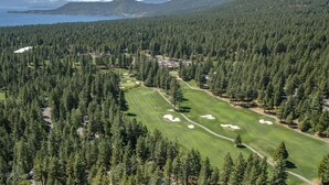 A golf course surrounded by dense forest and mountains.