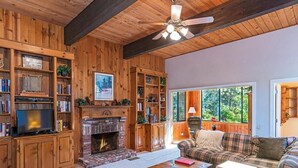 A cozy living room with wooden walls, a fireplace, a sofa, and a television.