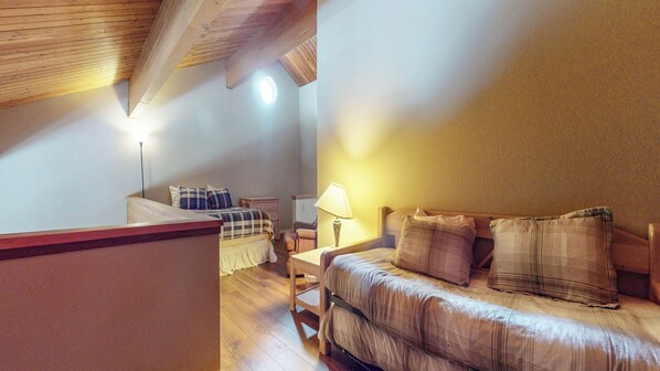 Un dormitorio con techo de madera, una cama con ropa de cama escocesa, una mesita de noche con lámpara y una pequeña mesa con silla.
