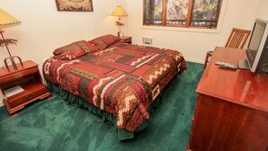 Een slaapkamer met een groot bed, een bureau met een computer, een lamp en een raam met uitzicht op bomen.
