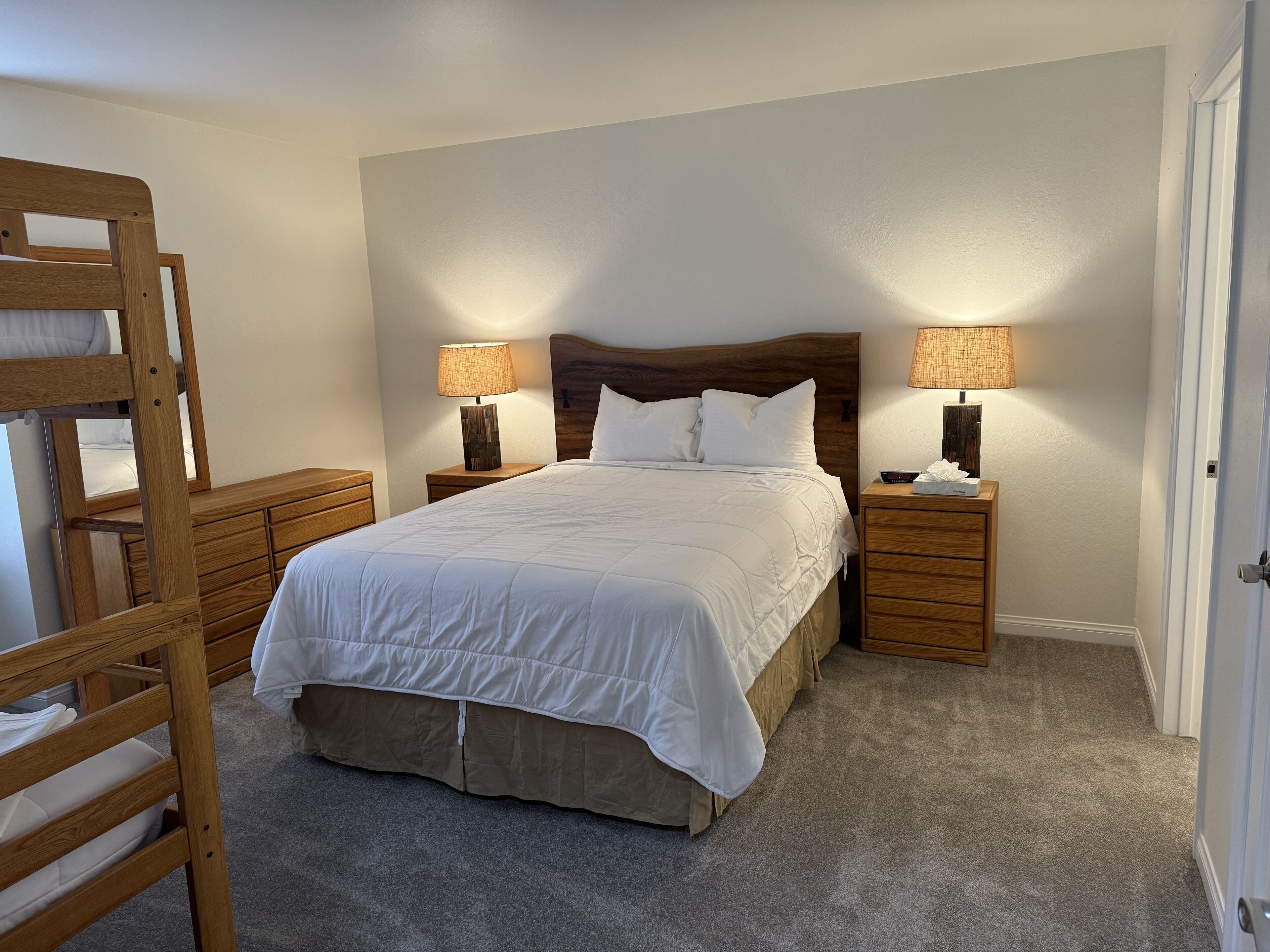 Un dormitorio con una cama, dos mesitas de noche, un aparador de madera y una litera.