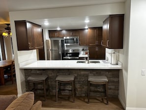 A modern kitchen with dark wooden cabinets, a white countertop, and a stone accent wall.