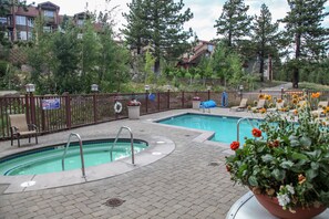 A swimming pool with a brick deck, surrounded by a fence, and a potted plant with flowers.