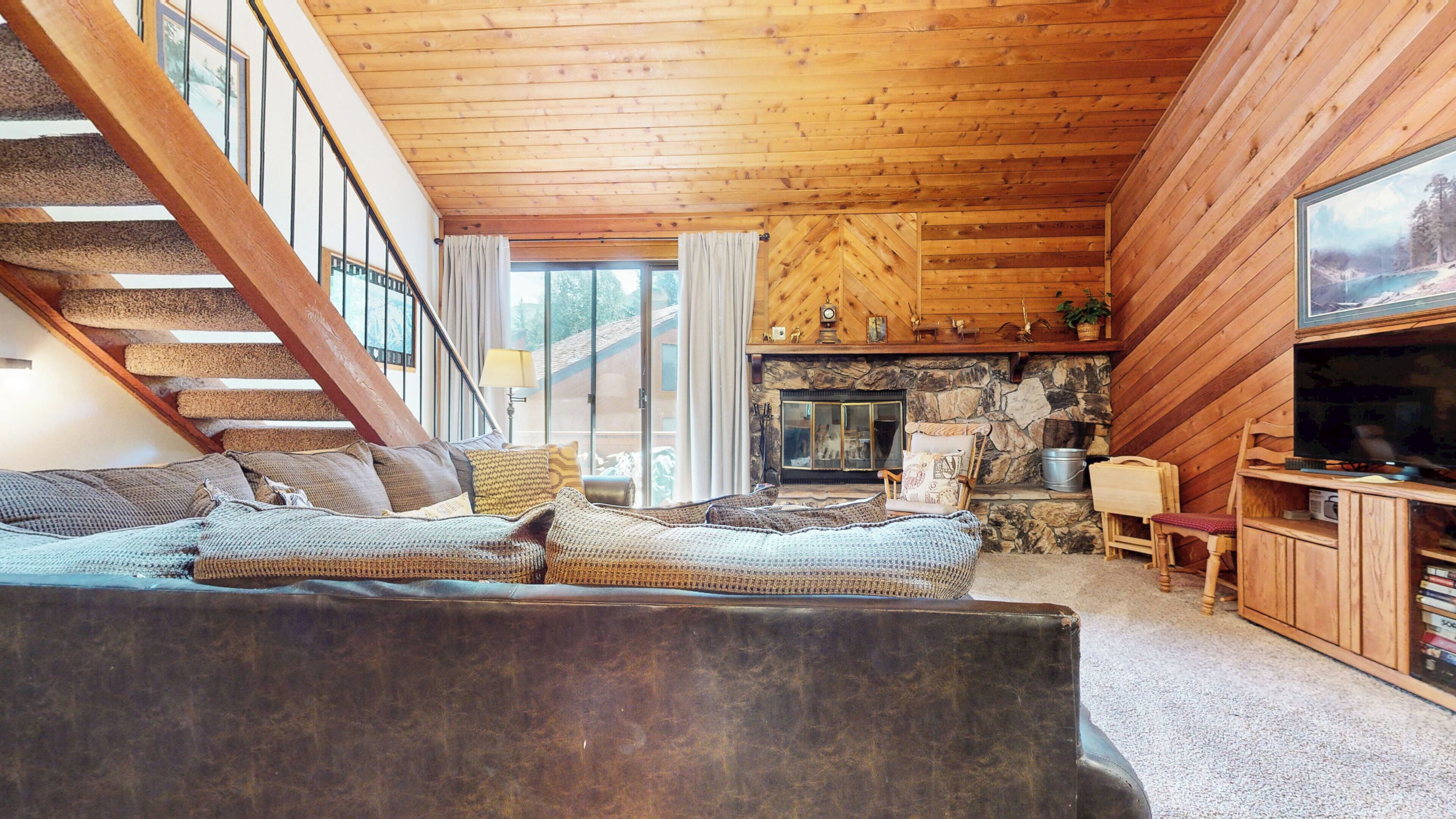 L’intérieur chaleureux d’un chalet avec un escalier en bois, une cheminée en pierre et une grande fenêtre.