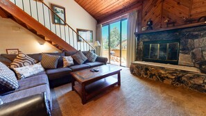 Cozy living room with a stone fireplace, comfortable sofa, and a wooden staircase leading to an upper level.
