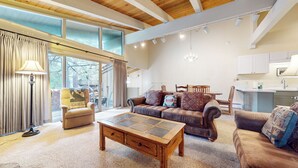 A spacious living room with a large window, a wooden ceiling, and a dining area with a kitchen in the background. - Bright Mountain Home, W/D, Near Bowling Alley & Kids Park, Summer Pool (Mammoth Lakes)