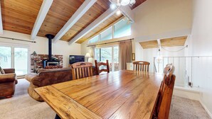 A spacious living room with a large wooden dining table, comfortable seating, a fireplace, and large windows allowing natural light. - Bright Mountain Home, W/D, Near Bowling Alley & Kids Park, Summer Pool (Mammoth Lakes)