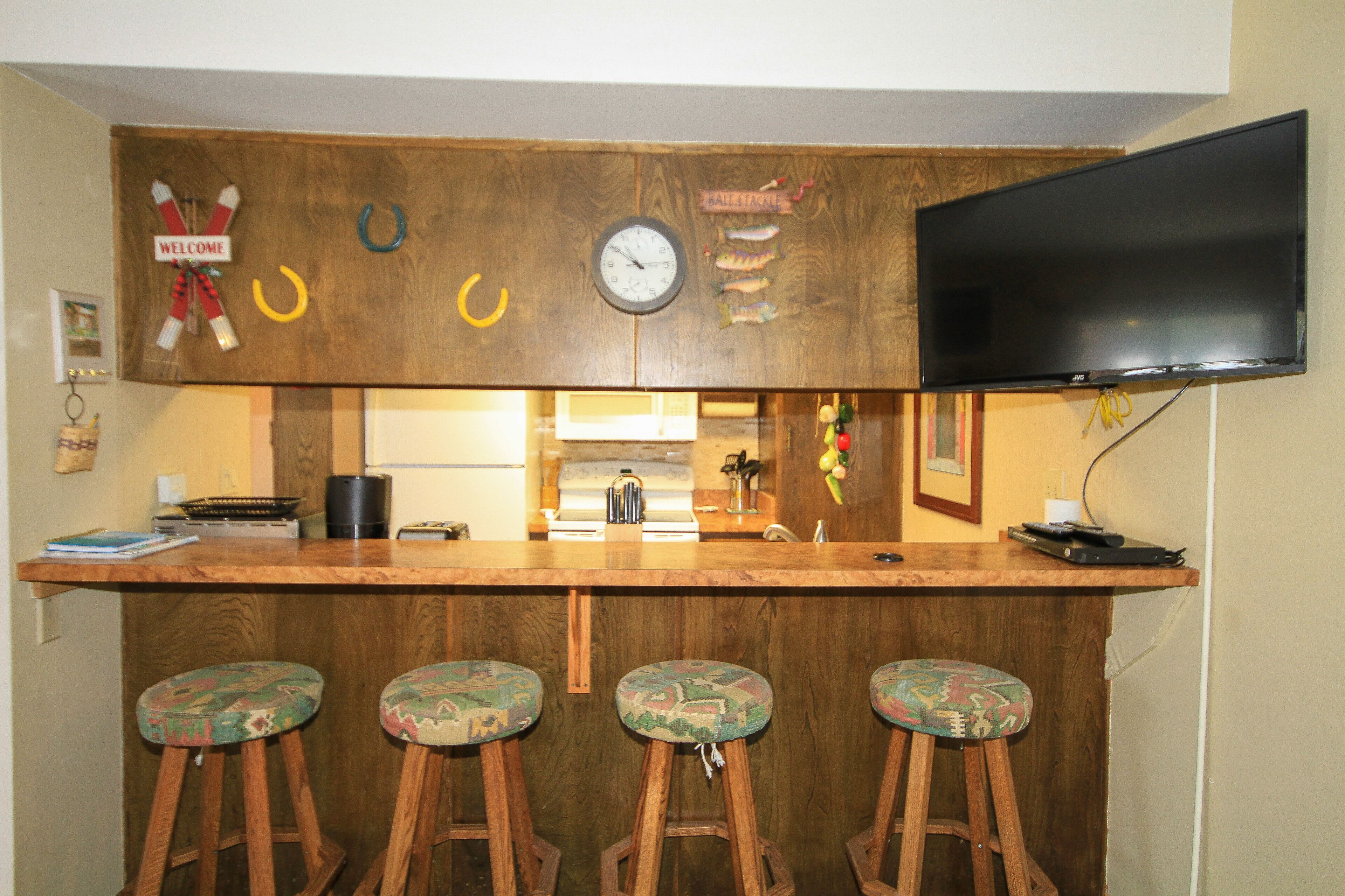 A bar area with wooden stools, a clock, and a television mounted on the wall.