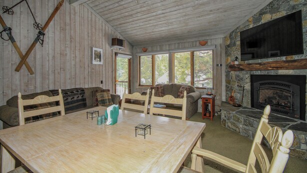 A rustic cabin interior with a wooden dining table, two sofas, a fireplace, and a stone wall. - Mountainback #12, 2 Bdrm, 3 Ba, Loft - Pet OK (Mammoth Lakes)