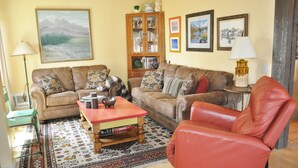 Un salon avec un canapé marron, un fauteuil rouge, une table basse et une bibliothèque.