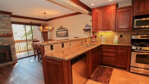 A kitchen with wooden cabinets, granite countertops, a built-in dishwasher, a stainless steel oven, and a stone fireplace. - Mammoth Ski & Racquet Club #34 (Mammoth Lakes)