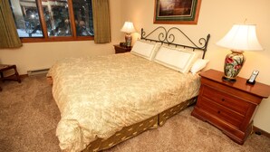A neatly made bed with a patterned bedspread, a bedside table with a lamp, and a nightstand with a vase. - Mountainback #49, Den (Mammoth Lakes)