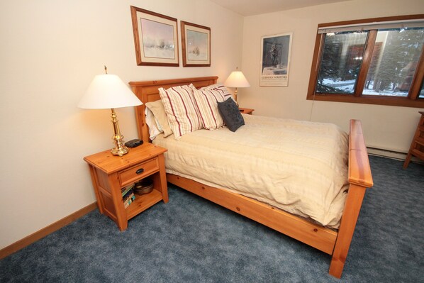 A bedroom with a wooden bed, two bedside tables with lamps, a bookshelf, and framed pictures on the wall.