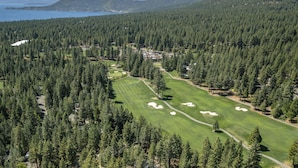 Golfkenttä, jonka ympärillä on tiheä metsä, ja josta avautuu näkymä järvelle ja taustalla kohoaville vuorille.