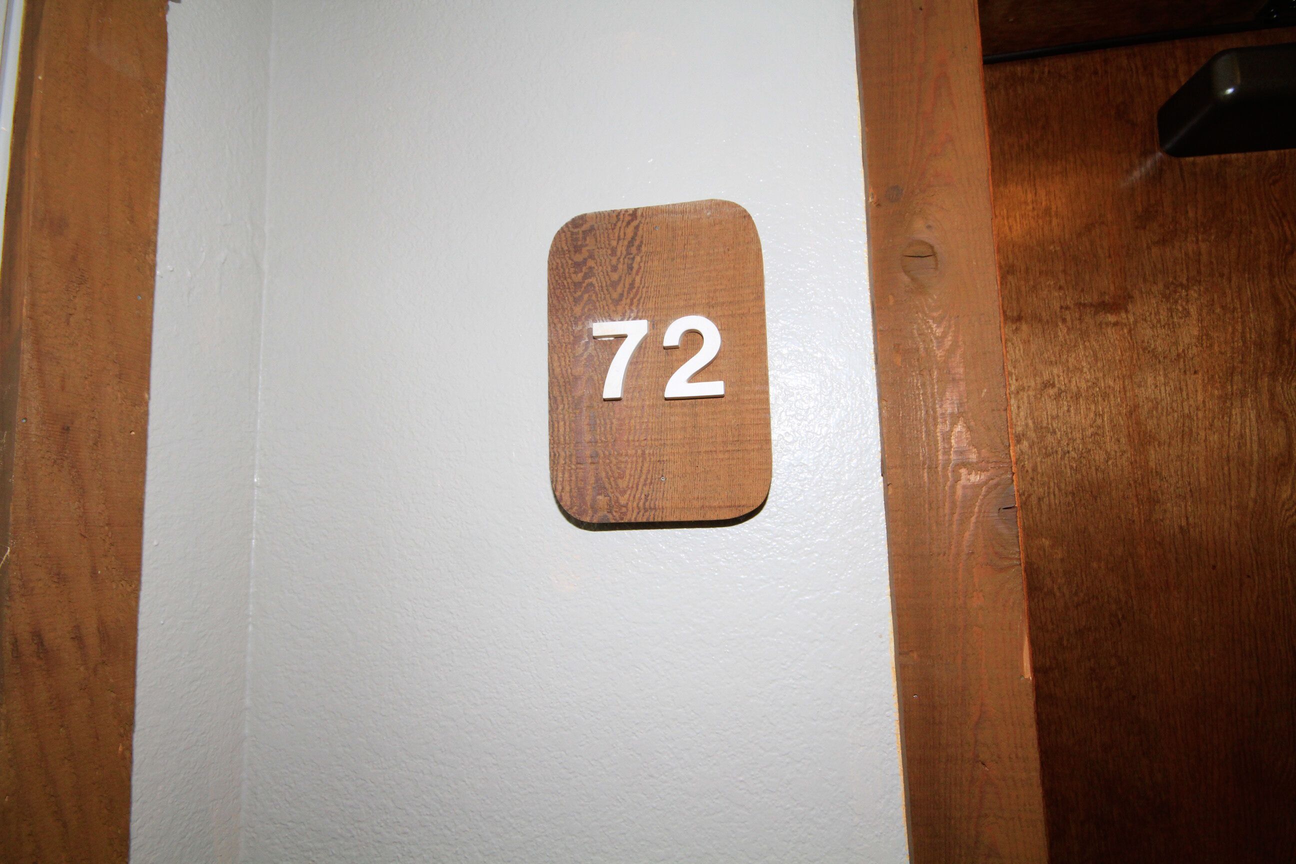 A wooden door with a white wall and a number '72' sign.