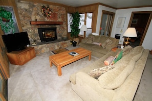 A living room with a stone fireplace, a wooden coffee table, a beige sofa, and a television on a wooden cabinet.