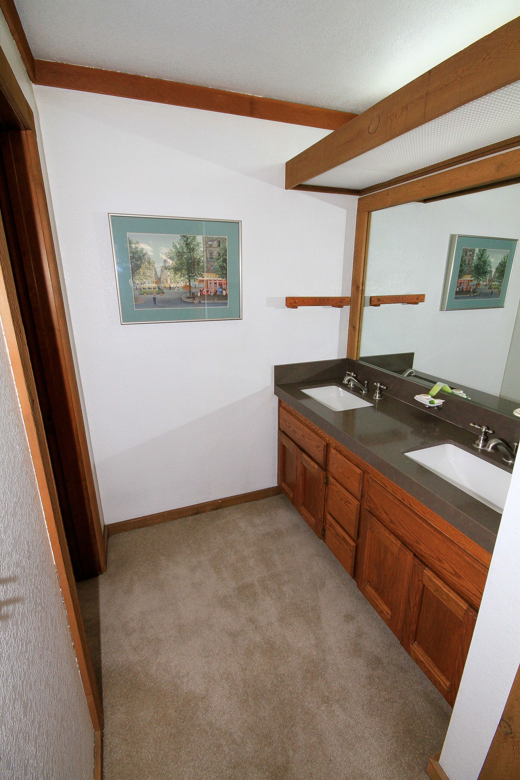 A bathroom with two sinks, wooden cabinets, and framed pictures on the wall.