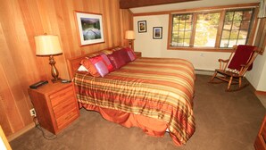 Quarto com uma cama grande, paredes de madeira, uma cadeira de balanço e uma janela com persianas.