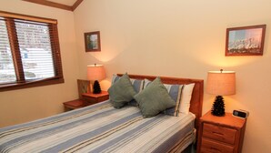 A neatly made bed with striped bedding, two bedside tables with lamps, a small pinecone decoration, and a framed picture on the wall. - Mountainback #105, Loft, Den (Mammoth Lakes)