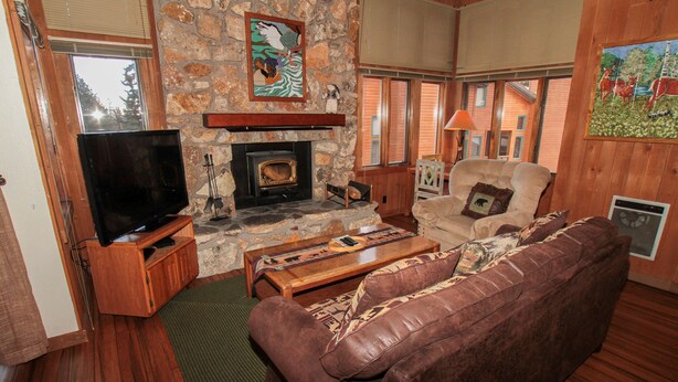 A cozy living room with a stone fireplace, a flat-screen TV, a leather sofa, and wooden flooring. - Mountainback #105, Loft, Den (Mammoth Lakes)