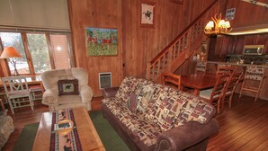 A cozy cabin interior with a wooden floor, a sofa, a dining table, and a kitchen area. - Mountainback #105, Loft, Den (Mammoth Lakes)